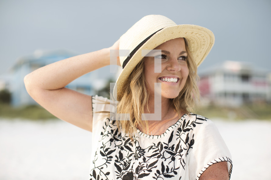 Smiling woman in a hat standing outside on the beach.