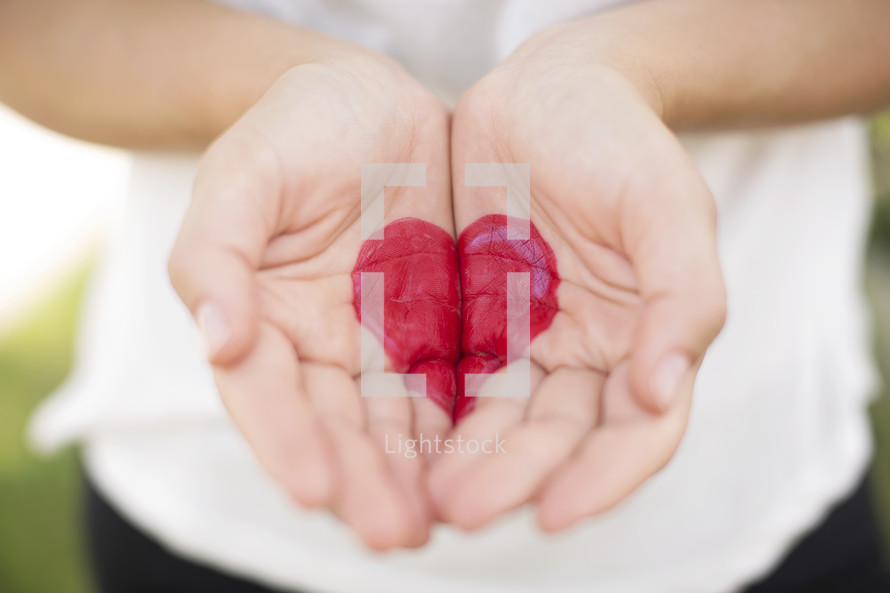 Two cupped hands painted with a red heart.