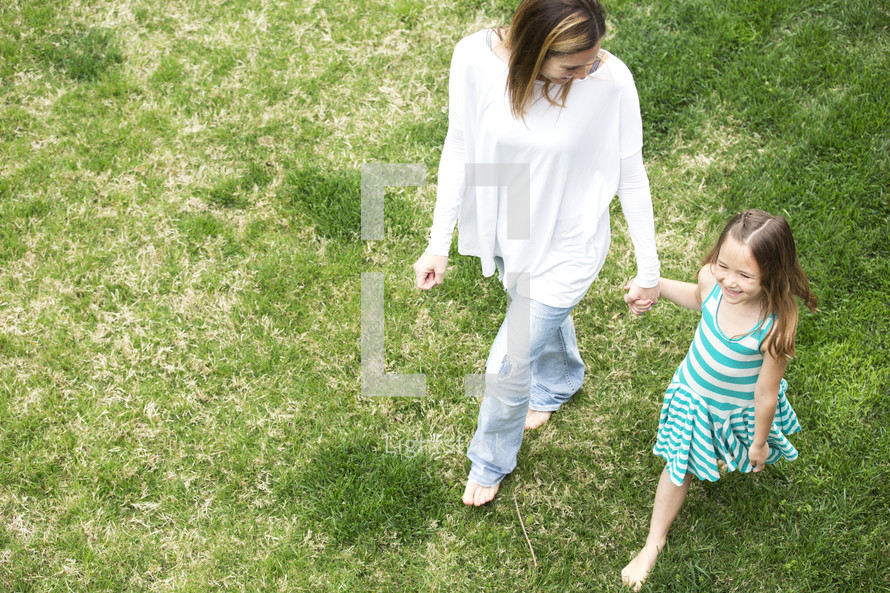 a mother and daughter walking holding hands through grass