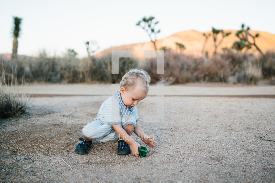a toddler playing with a toy car and desert landscape 