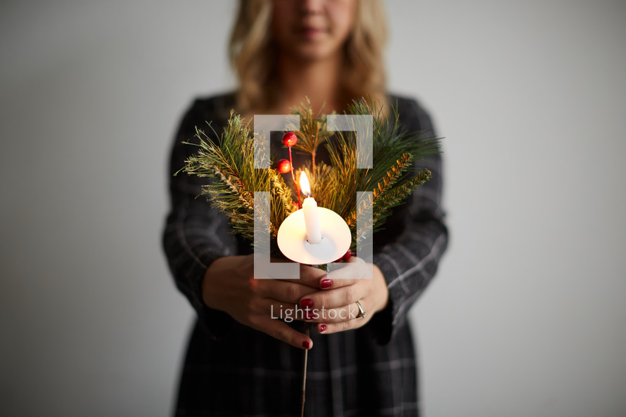 a woman holding a candle and Christmas greenery 