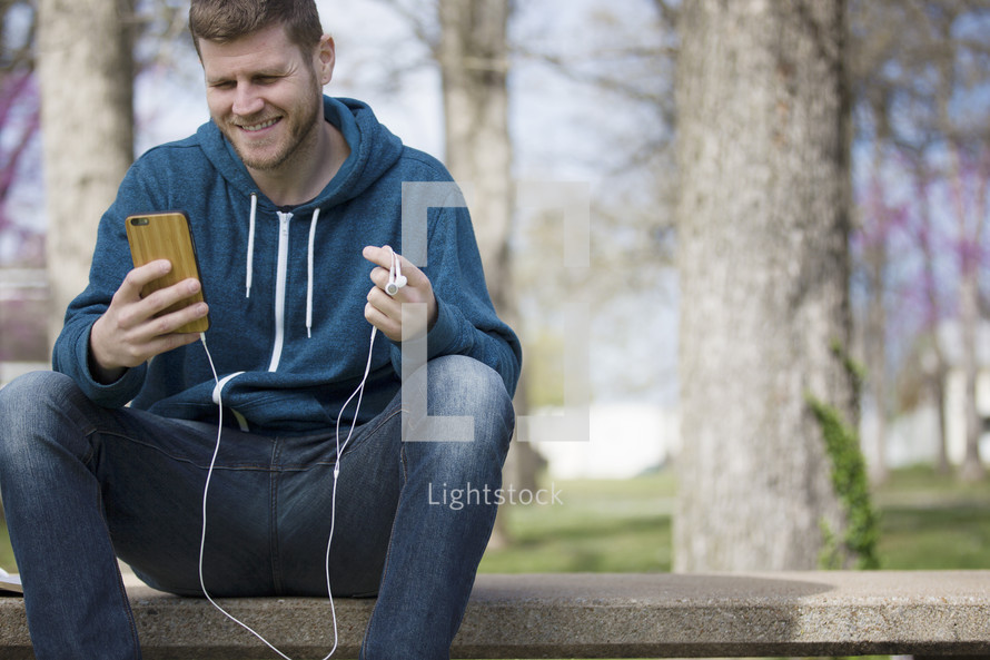 a man sitting holding an iPhone and earbuds 