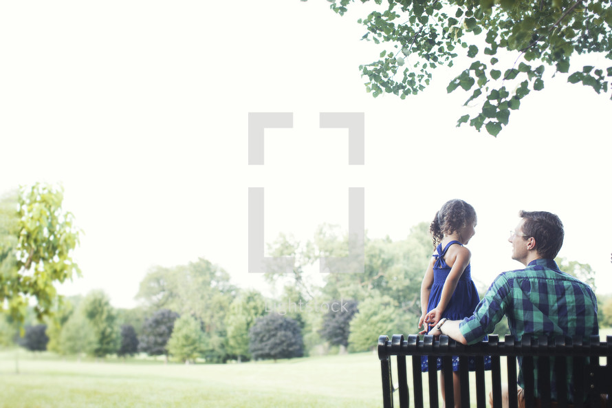 father and daughter sitting on a park bench outdoors 