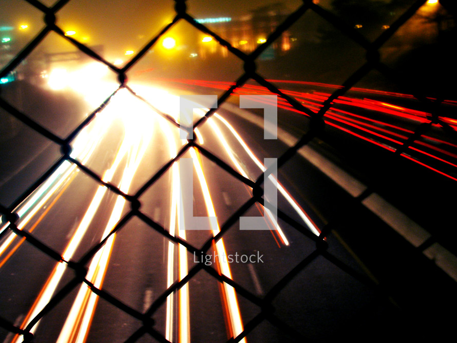 looking through a fence at the lights from moving cars at night