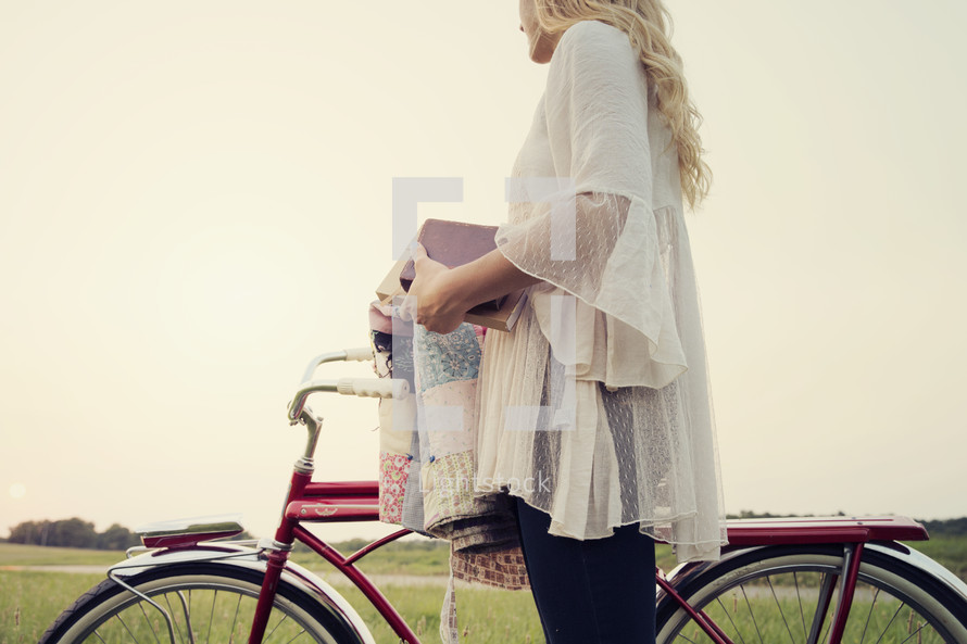 young woman standing next to a bicycle holding a quilt and a bible.