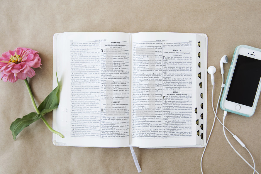 An open Bible between a pink flower and a cell phone.