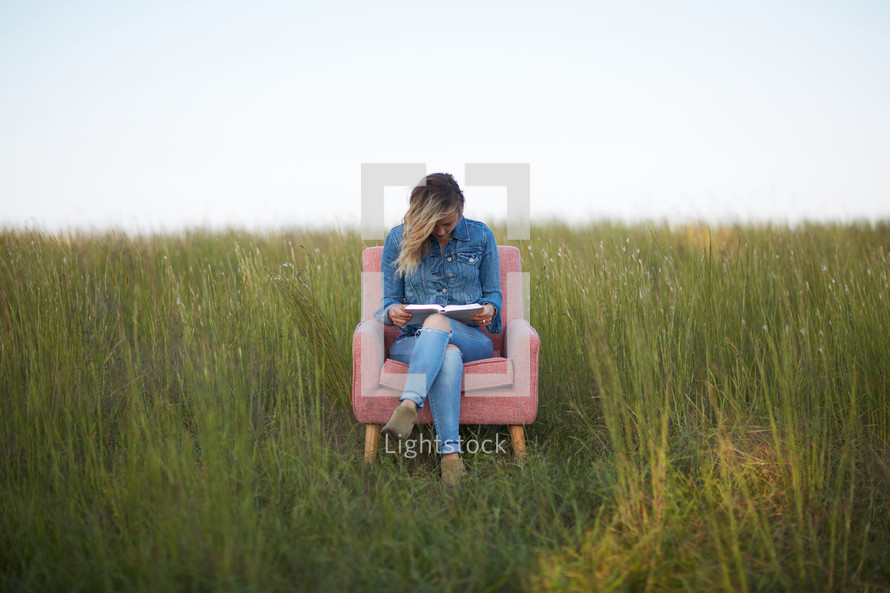 a woman sitting in a field reading a Bible 