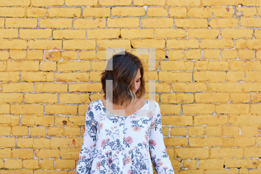 woman in a floral shirt standing in front of a yellow brick wall 