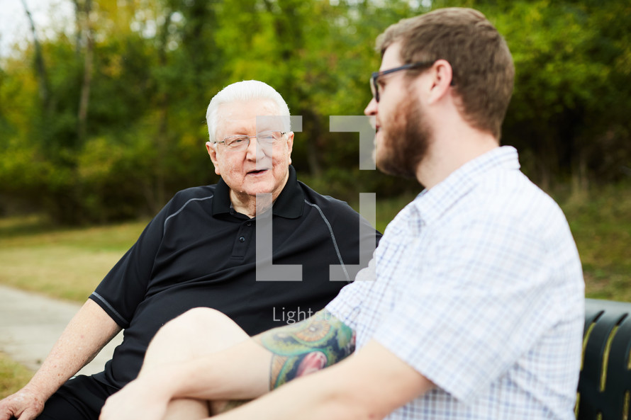 elderly man praying with and talking to a young man 