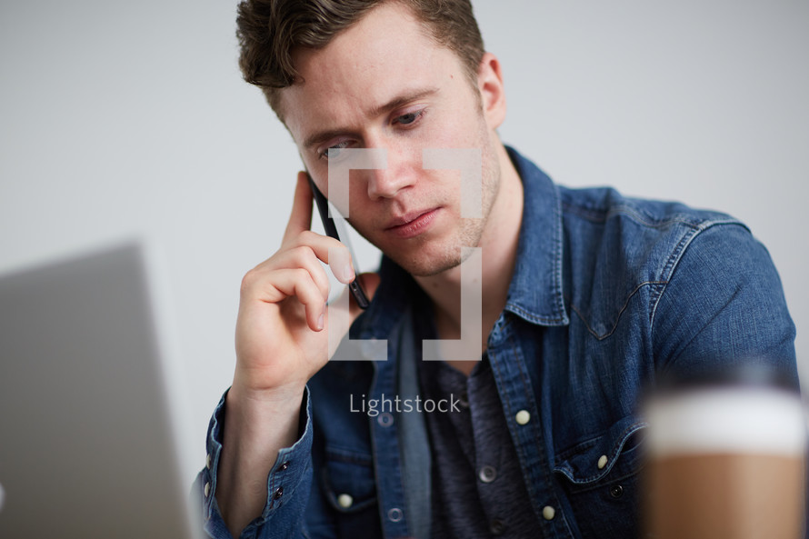 a man sitting behind a computer and talking on a cellphone 