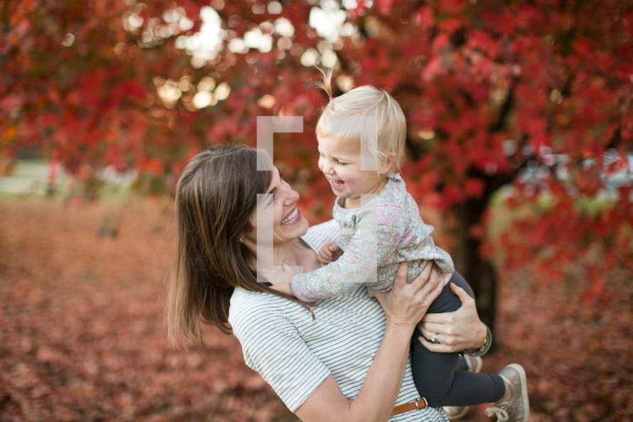 a mother holding a toddler girl outdoors in fall 