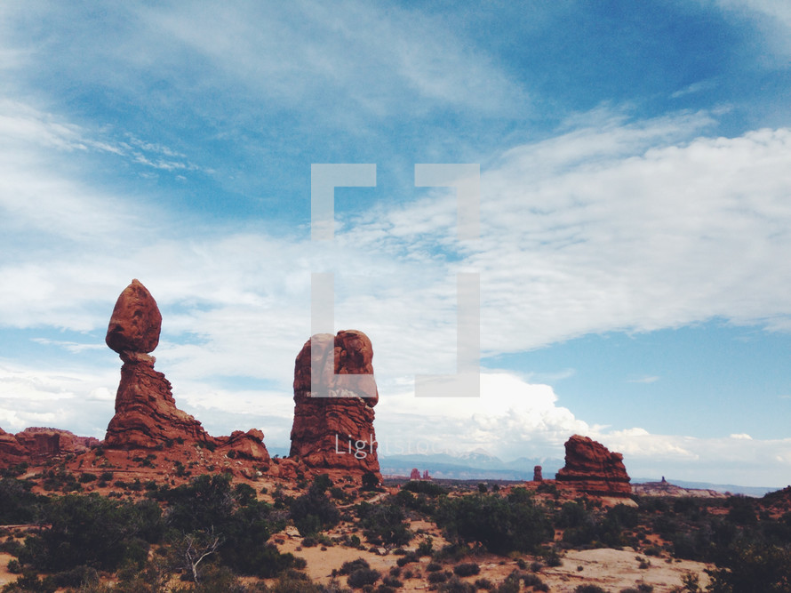 Large red rock formations in the desert against a blue sky and clouds.