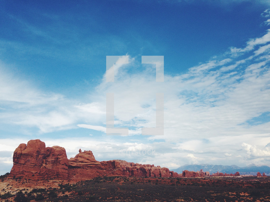 Enormous red rock formations in the desert against a blue sky and clouds.