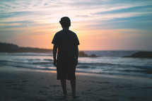 Silhouette of a young man standing on a beach at dusk | Youth | Facing Forward  | Praying | Sun | Faith | Children | Clouds | Courage | Determination | Mediation | Nature | Landscape | Peace