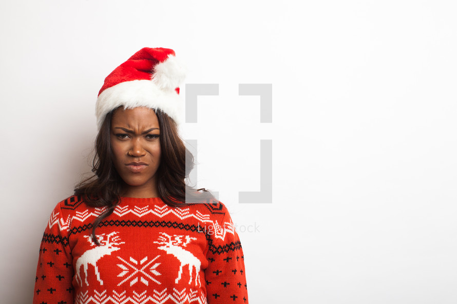 woman in an ugly Christmas sweater and santa hat with a frown 