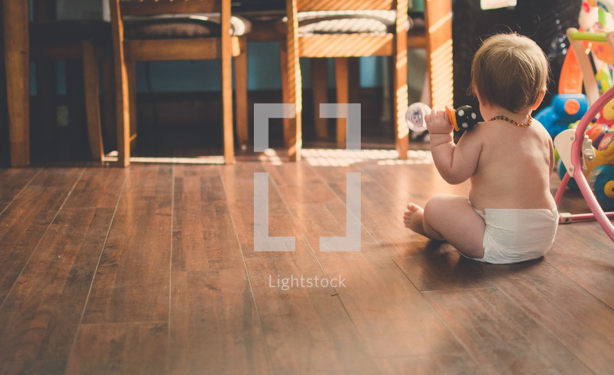 a baby in diapers sitting on a wood floor 