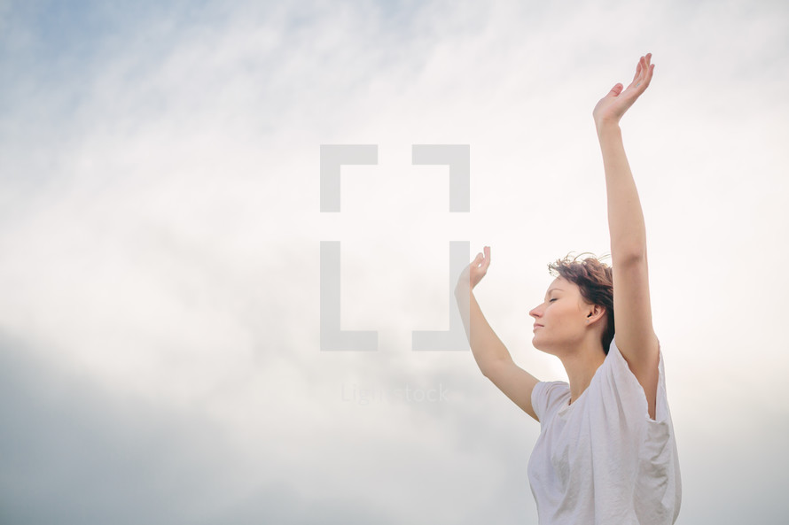 Woman standing outside with arms raised in praise.
