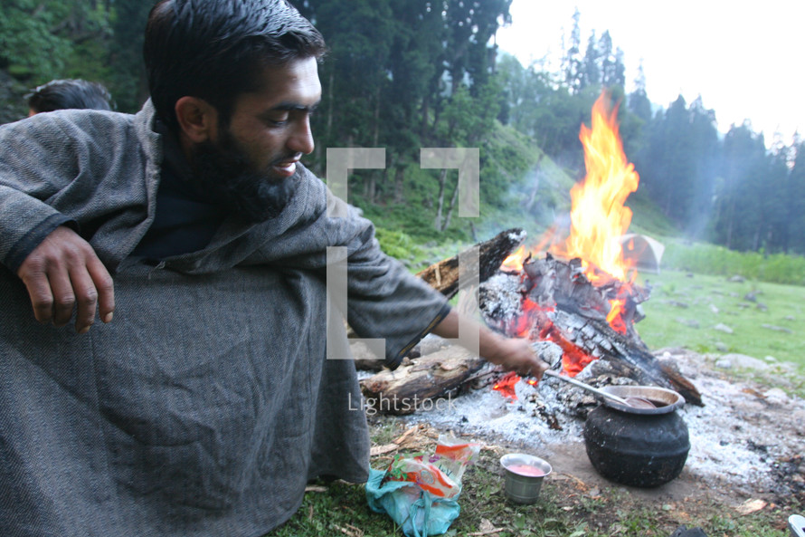 man cooking in a pot on an open fire 