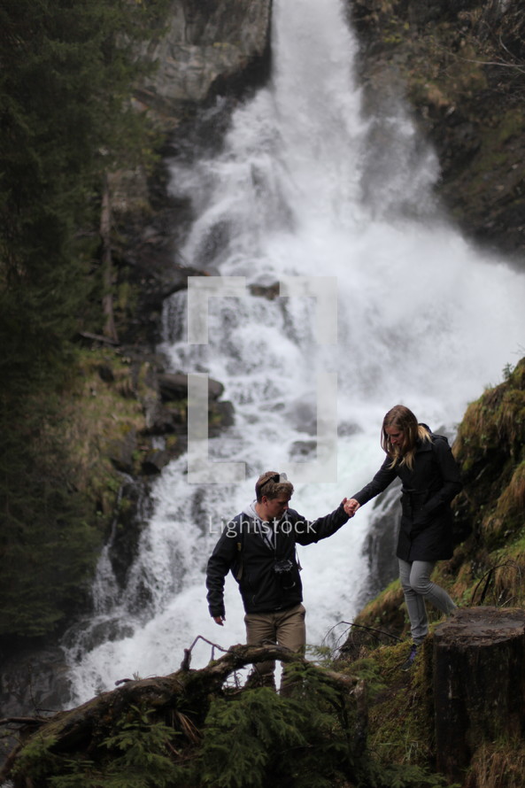 couple hiking up a mountain near a waterfall 