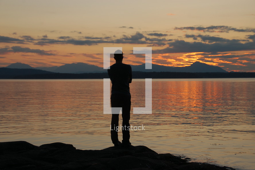 Silhouette of a man standing before a lake at dusk.