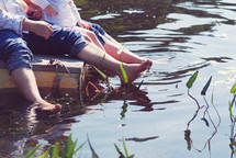 A family of three dips their feet in a lake.