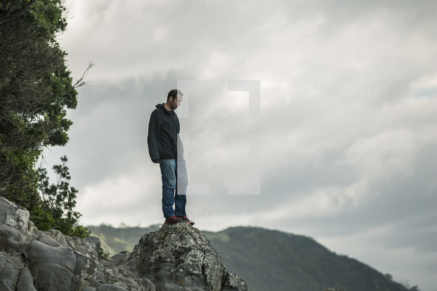 A man standing on a boulder on a mountain top.