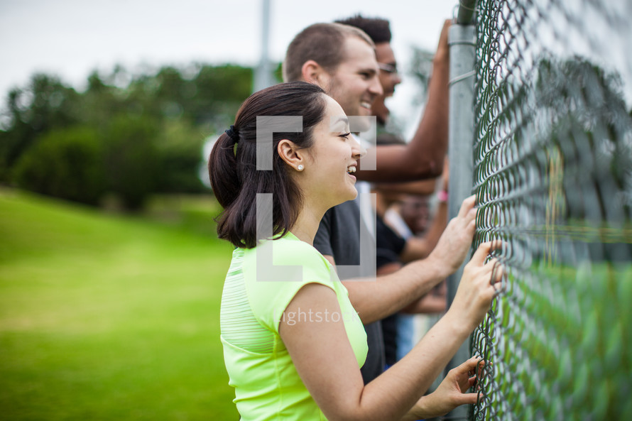 athletes standing on a sports field hanging onto a chain link fence 