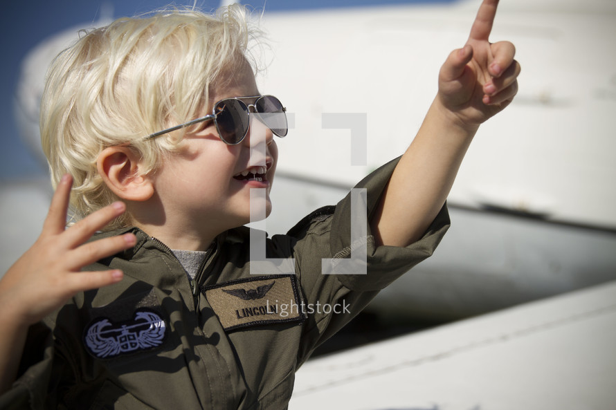 a boy child dressed in a fighter pilot uniform and aviator shades 