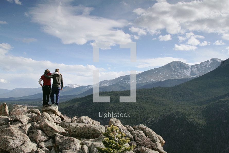 Embraced couple standing on rocks near a mountain range.
