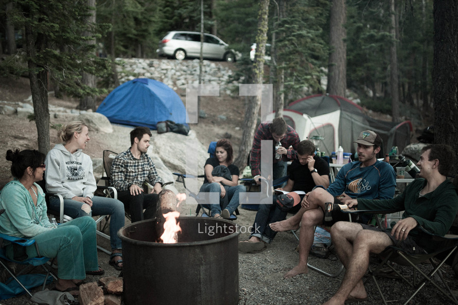 A group of campers sitting around a campfire in the forest.