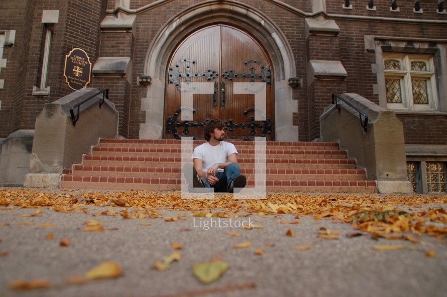 A man sits alone on the bottom step outside of a church