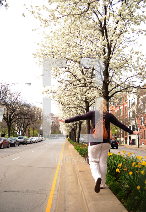 A woman walking along a street, balancing on the curb.