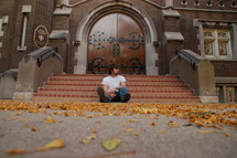 A man sits alone on the bottom step outside of a church