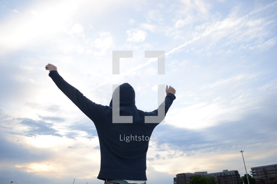 Back of a person in a hoodie outside with arms raised.