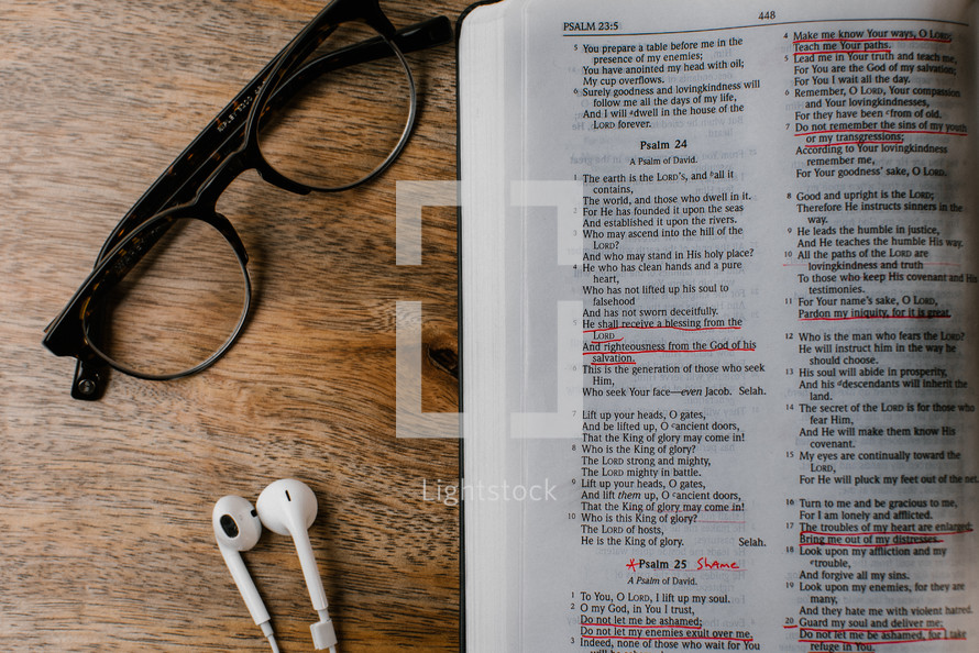 reading glasses, earbuds, and open Bible on wood table 