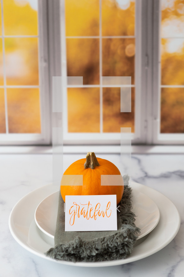 Thanksgiving place setting with the word grateful in front of a kitchen window