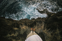 a man standing at the edge of a cliff looking down at the ocean 