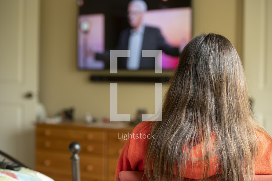 Woman watching a church service from home with Tv out of focus