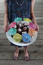 a girl holding a platter of brownies with cocktail umbrellas 