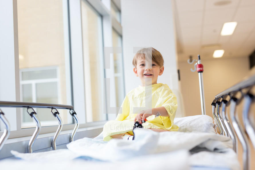a boy child in a hospital gown sitting  in a hospital bed 