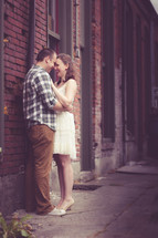 a couple embracing outdoors in front of a brick building 