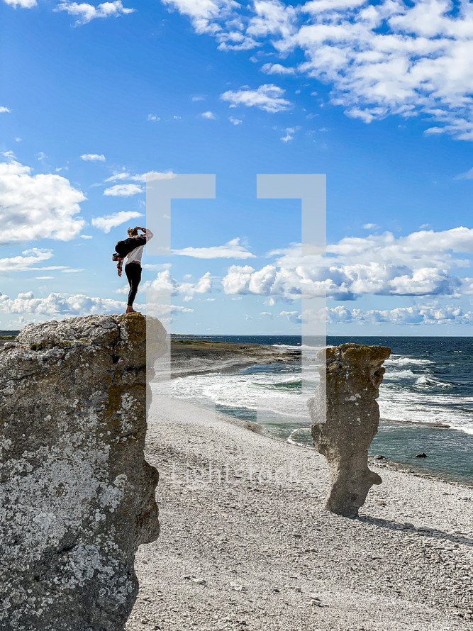 a man standing on a rocky cliff along a shore 