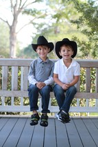 Young brothers sitting on a porch swing wearing cowboy hats