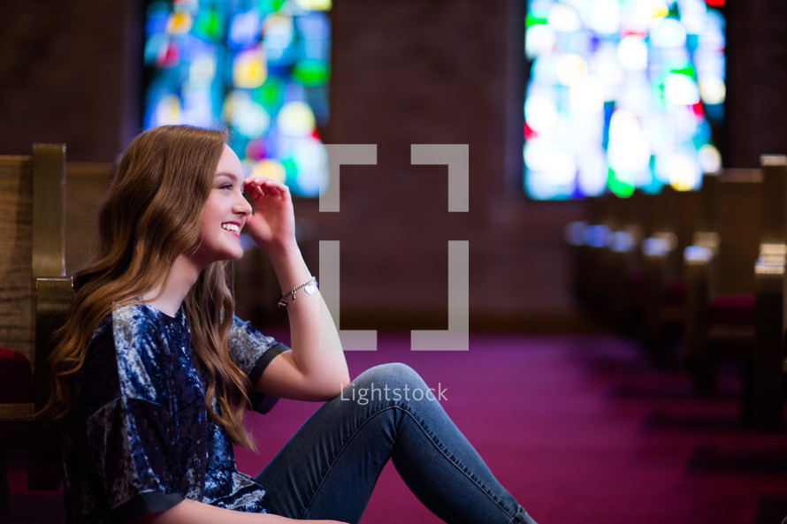 Young woman or teen sitting in aisle of a church with a joyful smile. 