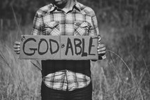 man holding a sign with the words God is able