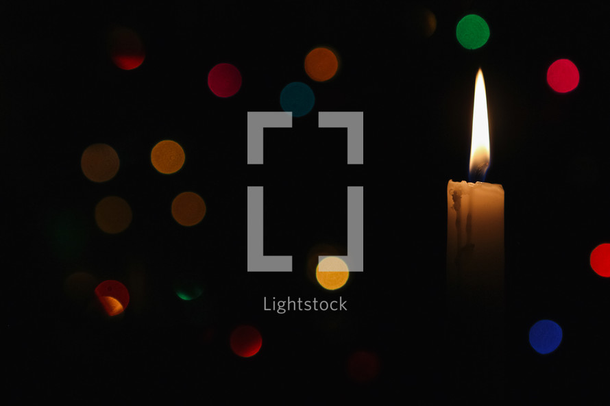 A single candle with flame in front of bokeh colorful Christmas lights