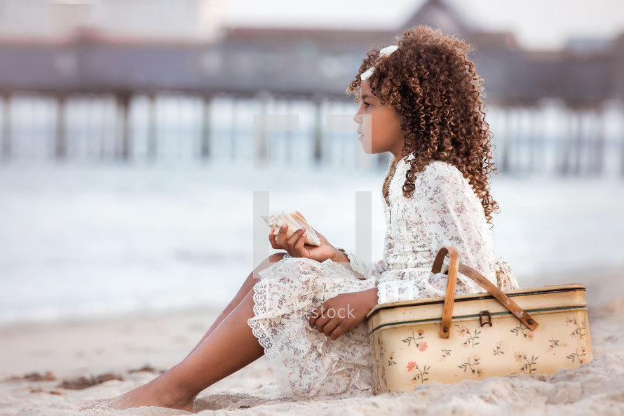 a girl with a basket sitting on a beach 