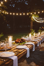 An long outdoor table set for an evening dinner party.
