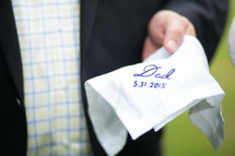 A groom holding a handkerchief embroidered with, "Dad, 5.31.2015."