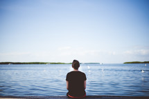 a woman sitting on a dock looking out at the water 